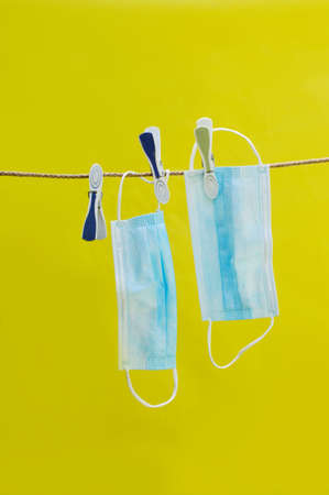 the vertical photo of the blue disposable masks and the clothespins handing on the rope over the yellow backgroundの写真素材
