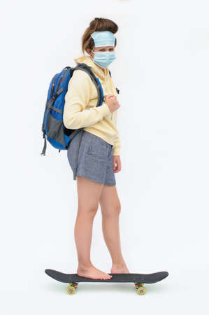 Vertical photo of the barefoot female student on the skate board with the disposable masks of the face over the white backgroundの写真素材
