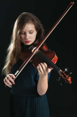 Long haired teen girl with a red lipstick  playing a violin over the dark backgroundの写真素材
