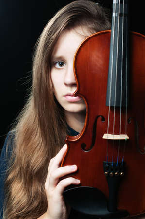 A portrait of a teeage girl with a violin covering a half of her face over the dark backgroundの写真素材