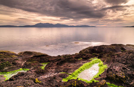 View to Isle of Arran from rocky shore at Portencross in Scotlandの写真素材
