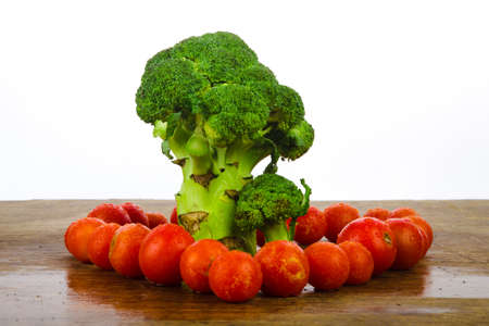 broccoli like a tree standing on a wooden texture on a white background, surrounded by red cherry tomatoesの写真素材