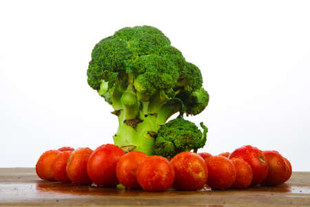 broccoli like a tree standing on a wooden texture on a white background, surrounded by red cherry tomatoesの写真素材