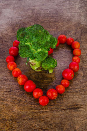 broccoli like a tree standing on a wooden texture, surrounded by red cherry tomatoes in the form of heart, healthy food.の写真素材