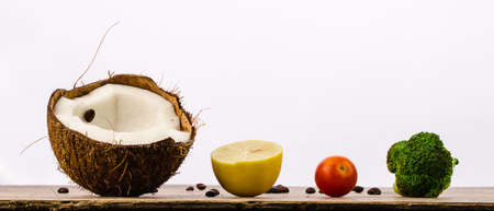 train of coconut, lemon, cherry tomatoes and broccoli on a wooden table on a white background decorated with coffee beansの写真素材
