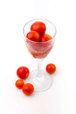 Photo of glass with tomato juice and a couple of cherry tomatoes in it, and few tomatoes near the glass on a white backgroundの写真素材