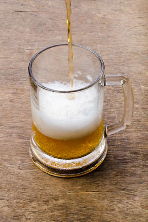 Beer being poured into beer glass creating foam and bubbles on wood textureの写真素材
