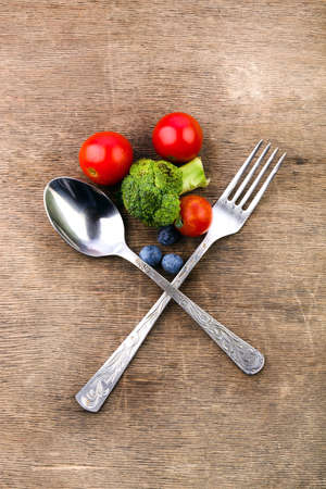 spoon and fork crosswise on a wooden background in front of cherry tomatoes and broccoli, vegetarian breakfast, healthy foodの写真素材