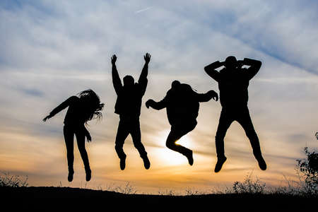 Silhouette of a group of four happy people jumping at sunset, happy team of 4 guys and 1 girlの写真素材