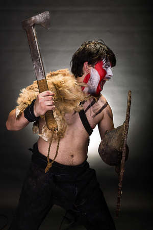 studio portrait in profile of a man in war paint with an ax in one hand and a shield in the other handの写真素材