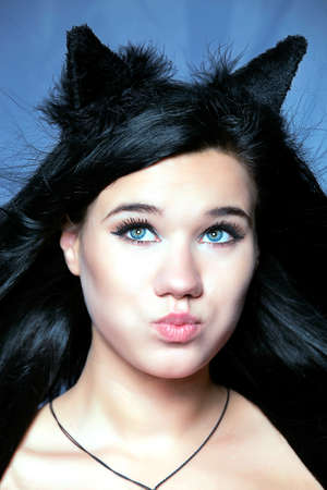 Close studio portrait of a girl with cat ears, girl with beautiful blue eyes inflates cheeks and...