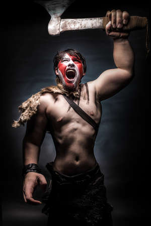Painted image of man in war paint, with an ax in his hand, a warrior brandishing an ax furiously screaming, barbarian of ancient times, Viking and savage.の写真素材