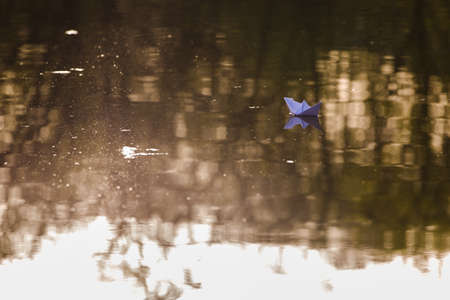paper boat sailing on water surface at sunset