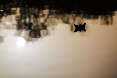 paper boat sailing on water surface at sunsetの写真素材