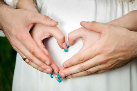 heart shaped pregancy in a flowering poppy field outdoors, close up heart shaped handsの写真素材