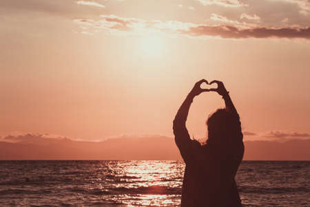 silhouette of young woman making a hand shaped heart at sunrise on the beach.の写真素材