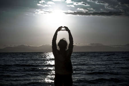 silhouette of young woman making a hand shaped heart at sunrise on the beach.の写真素材