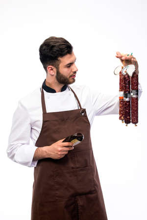 young cheaf with salami in one hand and knife in other hand, sausage department advertisingの写真素材