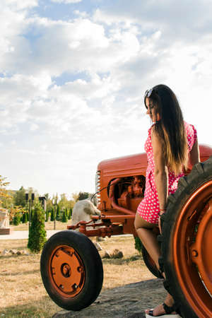 young girl in a pink dress with polka dots near the tractor, background.の写真素材