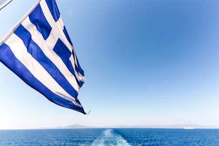 Ferry boat in Greece view on sea with cruise ship trail, traces on water and greek flagの写真素材