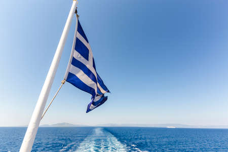 Ferry boat in Greece view on sea with cruise ship trail, traces on water and greek flagの写真素材
