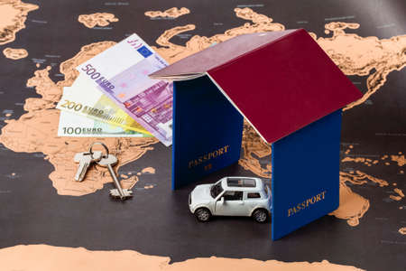 passports in the form of a house, a toy machine, money and keys on the background of a geographical map, a concept of tourism or traveling around the worldの写真素材