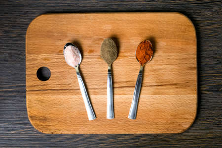 spoons with spices (red paprika, black pepper, Himalayan salt) on a kitchen wooden board, against a background of dark wood, flat lay imageの写真素材