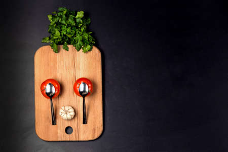 cartoon funny surprised face of tomatoes, spoons, garlic and parsley lined on the kitchen wooden board, with space for text, the concept of creative and fun cooking, flat lay imageの写真素材