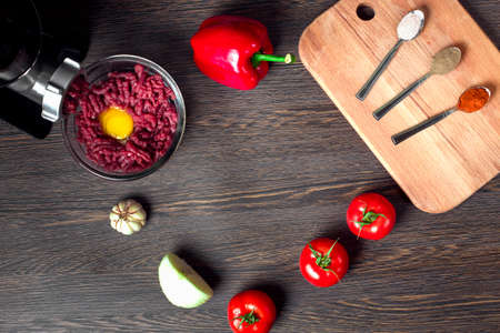 still life of electric meat grinder, tomato, spices, paprika and onion on a wooden background, flat lay image with space for textの写真素材