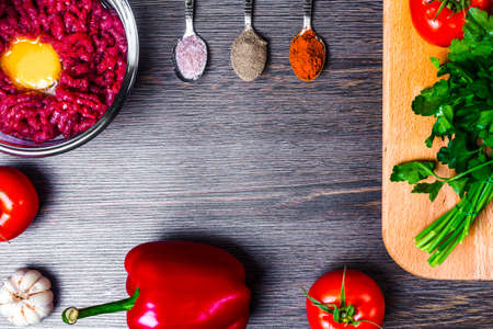 pepper paprika on a wooden background near parsley, garlic, minced meat, tomato and spoons with spices, the concept of cooking in the kitchen with space for textの写真素材