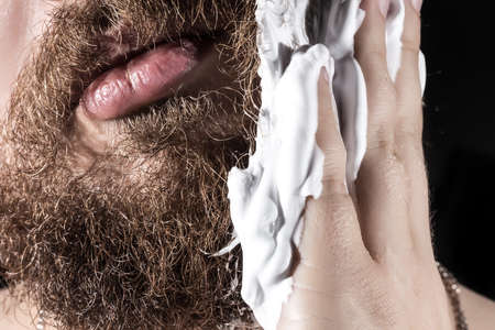 a man young in shaving foam, preparing to remove hair, part of a face close-upの写真素材