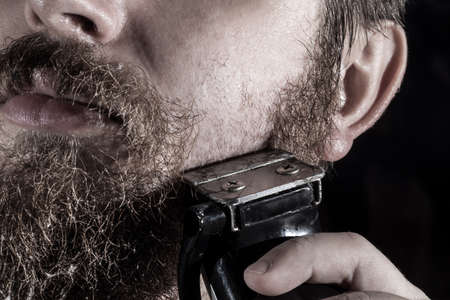man shaves his beard with a typewriter, photo close-up on a black backgroundの写真素材