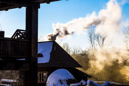wooden house with a submerged stove and smoke leaving in the sky on a sunny winter dayの写真素材