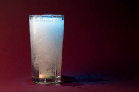 transparent glass with mineral water and effervescent tablet, on a red background with space for...