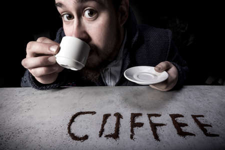 portrait of a man with big eyes is drinking coffee while looking into the cameraの写真素材