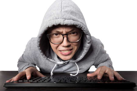 a perturbed programmer with glasses and a hood in front of the keyboard looking at the camera, isolated on white backgroundの写真素材