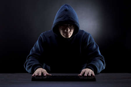 hacker in the hood and glasses in front of a keyboard on a dark background