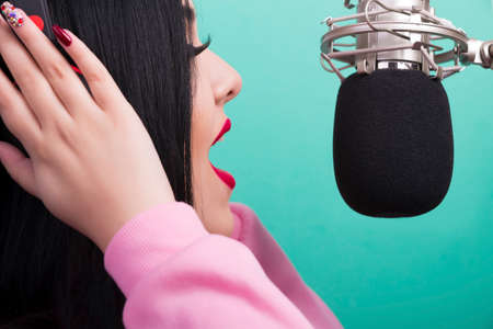 closeup portrait of a singing girl with red lips and studio microphone on azure backgroundの写真素材