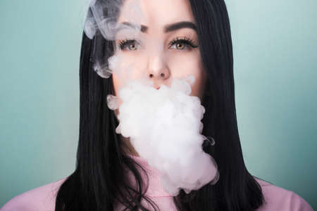 portrait of a girl who smokes an electronic cigarette and releases smoke from his mouth on azure...