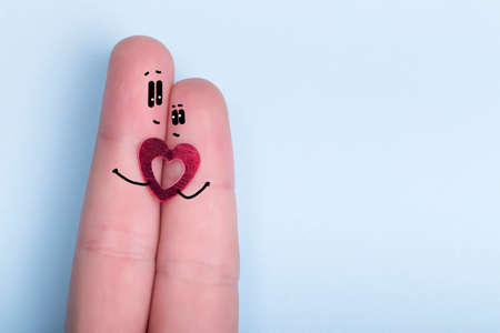 fingers with a decorative heart and painted faces on a blue background, the concept of a couple in love, postcard for  Valentine's Dayの写真素材