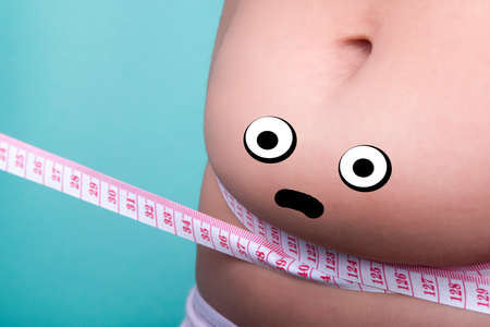 personified with shocked eyes and sad smile female belly with overweight, wrapped with a measuring tape, the concept of proper nutrition and diet for weight lossの写真素材
