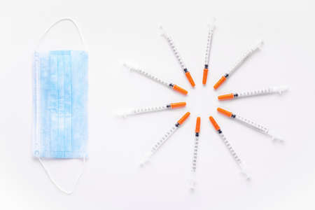 insulin syringes near to a protective blue mask, on a white background, concept of medical screensaverの写真素材