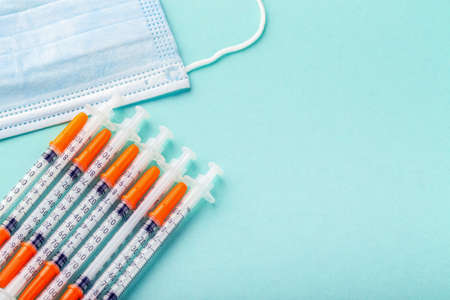 insulin syringes near the protective mask on a blue background, medical conceptの写真素材