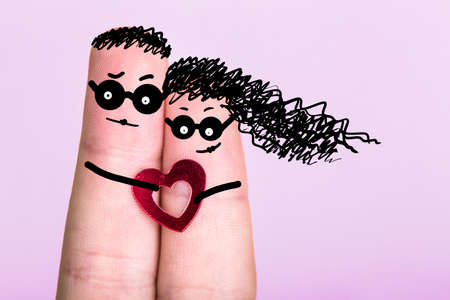 fingers with painted faces in glasses on a pink background, concept of an engaged couple, blank for Valentine's Dayの写真素材
