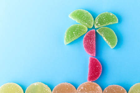 jelly colored jelly slices in the shape of a palm tree and the beach on a blue background, vacation conceptの写真素材