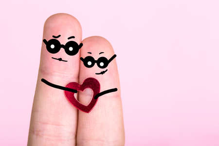 fingers with painted faces in glasses on a pink background, concept of an engaged couple, blank for Valentine's Dayの写真素材