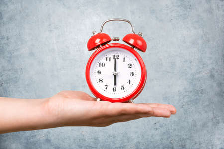 red clock with alarm on hand  on a concrete wall background, wake up concept in the morningの写真素材