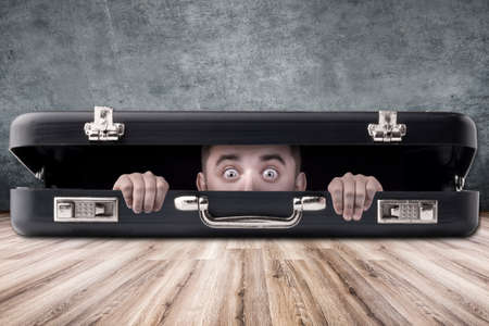 a man with big eyes looks out of a black case, the subject in the middle of the roomの写真素材