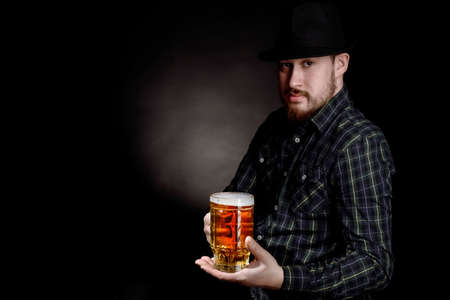 bearded man in a hat with a glass of beer on a black backgroundの写真素材