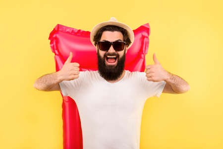studio portrait of a bearded man in sunglasses and a panama hat, the guy is  showing likes, standing on background a pink inflatable swimming mattress, concept of vacation at sea and summer moodの写真素材